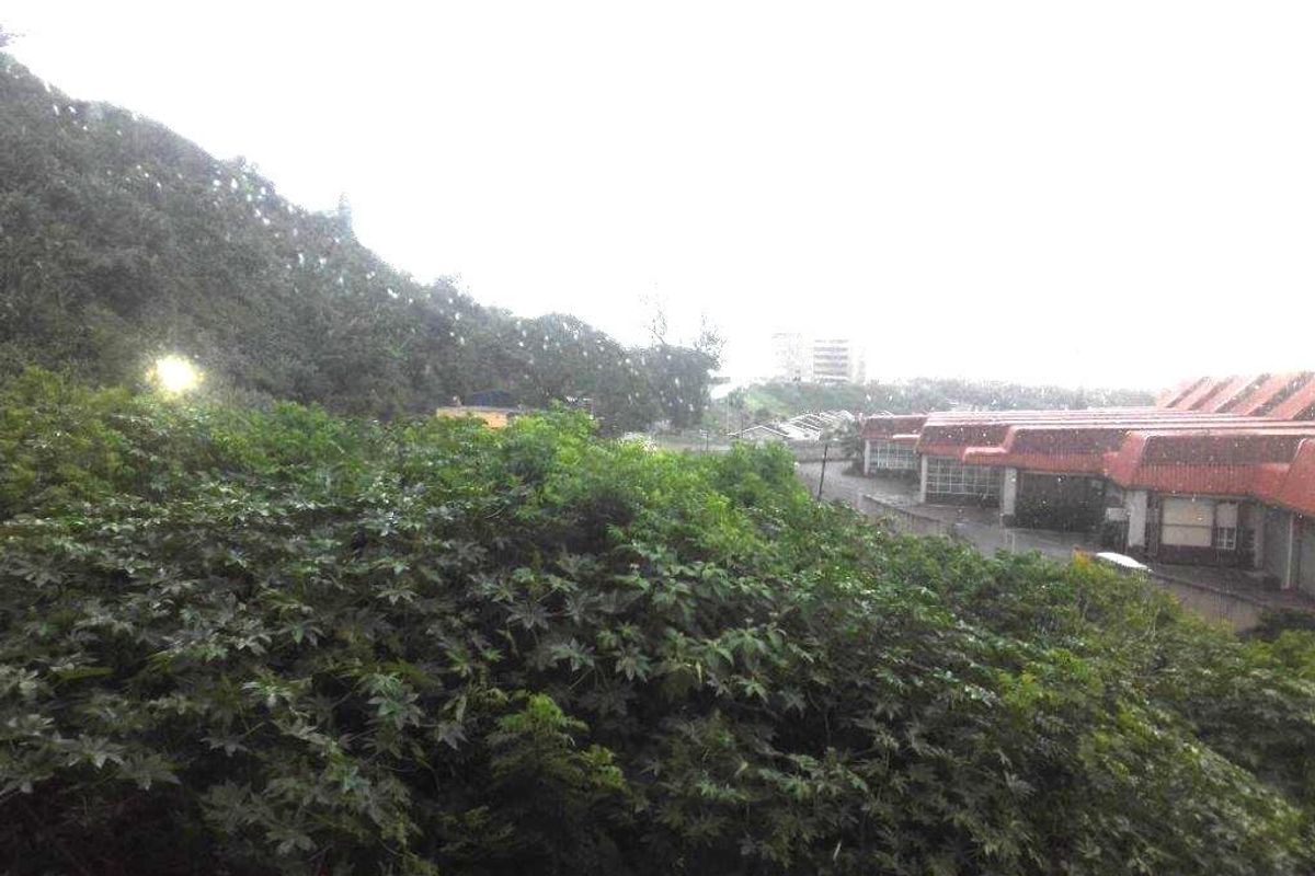 An elevated view overlooking lush greenery and a neighbouring residential complex with red-tiled roofs.