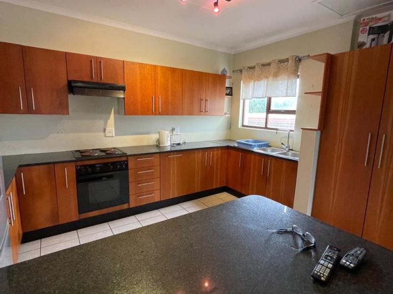 Functional kitchen featuring wooden cabinetry, granite countertops, built-in oven and hob, and tiled flooring with ample storage space.