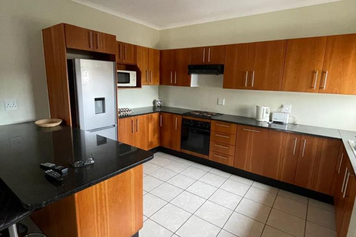 A functional kitchen featuring wood-finish cabinetry, granite countertops, a breakfast bar, and integrated appliances with tiled flooring and modern track lighting.
