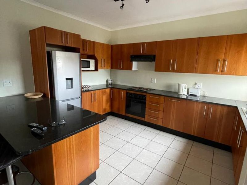 A functional kitchen featuring wood-finish cabinetry, granite countertops, a breakfast bar, and integrated appliances with tiled flooring and modern track lighting.