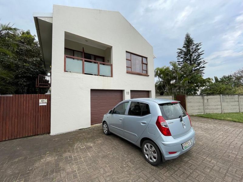 Front elevation of a two-story apartment building featuring a double garage, paved driveway, and an upper-level balcony.