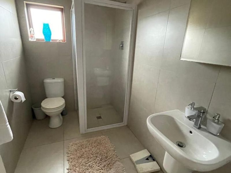 A functional bathroom featuring a shower enclosure, pedestal basin, toilet, and neutral wall and floor tiling.