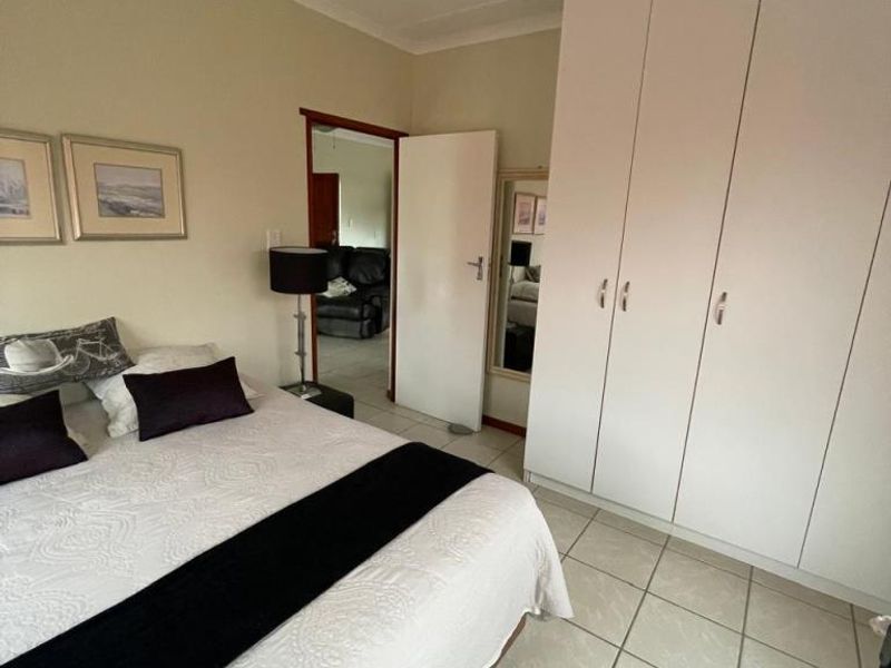 A bedroom featuring tiled flooring, built-in cupboards, and a ceiling fan, with an adjoining view into the living area.