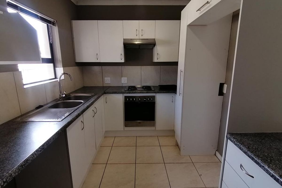 A functional kitchen featuring white cabinetry, dark laminate countertops, built-in oven, hob, extractor fan, and tiled flooring.