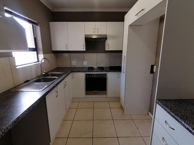 A functional kitchen featuring white cabinetry, dark laminate countertops, built-in oven, hob, extractor fan, and tiled flooring.