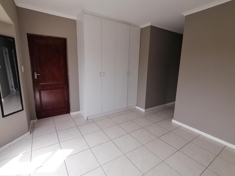 A clean, empty bedroom featuring neutral wall tones, white tiled flooring, and ample built-in cupboard storage space.