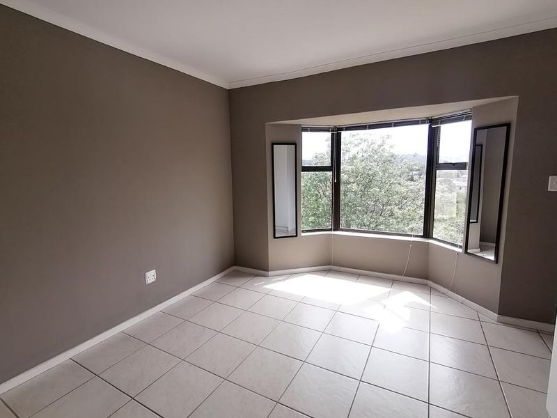 A bright, empty bedroom featuring neutral wall tones, large bay windows providing natural light, and clean ceramic floor tiling.