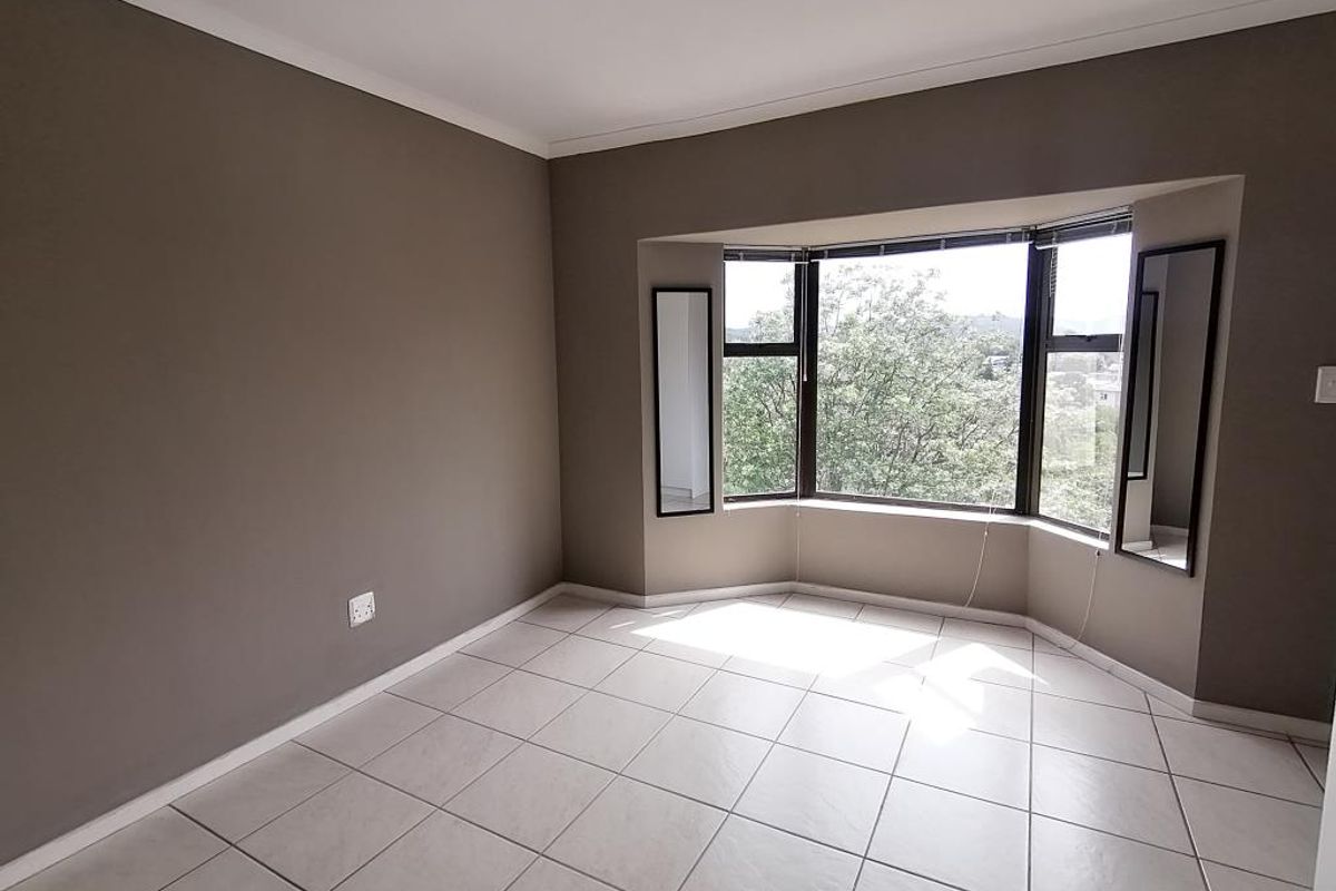 A bright, empty bedroom featuring neutral wall tones, large bay windows providing natural light, and clean ceramic floor tiling.