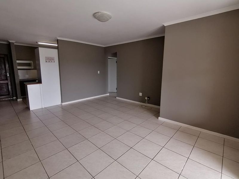 An open-plan living area featuring neutral grey walls, ceramic floor tiles, and a breakfast bar leading into the kitchen space.