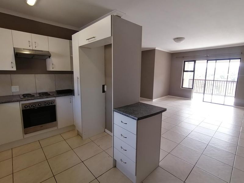 Open-plan kitchen and living area featuring tiled flooring, built-in cabinetry, integrated oven and hob, and direct access to a balcony through sliding doors.