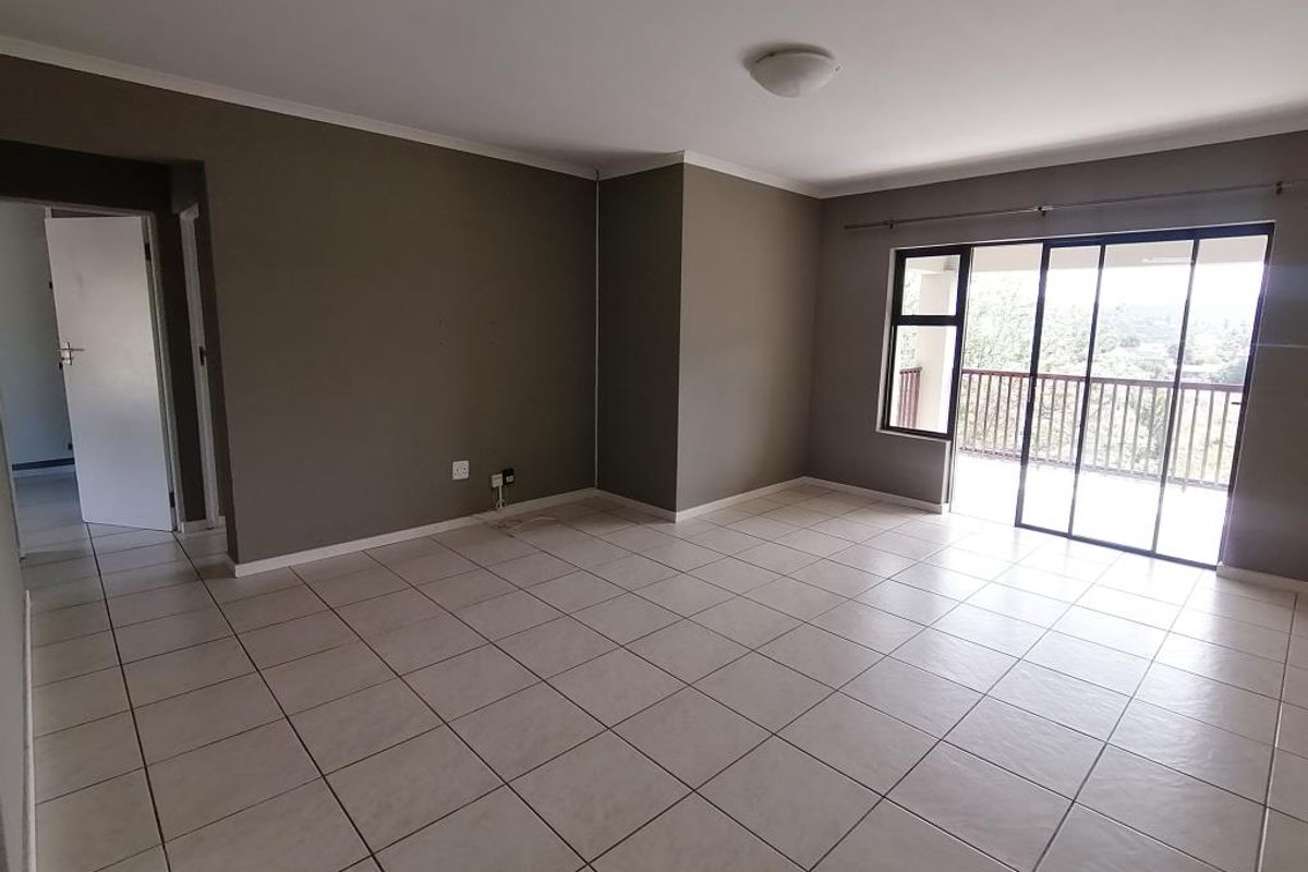 Spacious, empty living area featuring neutral wall tones, tiled flooring, and large sliding glass doors providing access to an outdoor balcony.