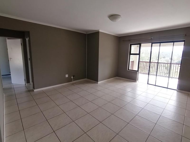 Spacious, empty living area featuring neutral wall tones, tiled flooring, and large sliding glass doors providing access to an outdoor balcony.