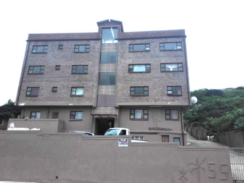 Exterior view of a multi-story apartment building featuring a brick facade, aluminum-framed windows, and a secure boundary wall with gated access.