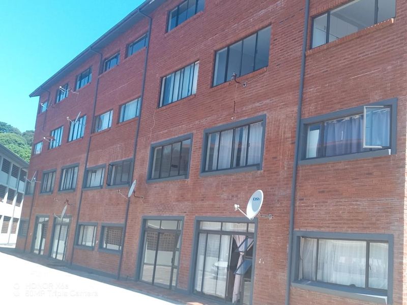 Exterior view of a multi-story apartment building featuring a red brick facade with dark-framed windows and multiple satellite dish installations.