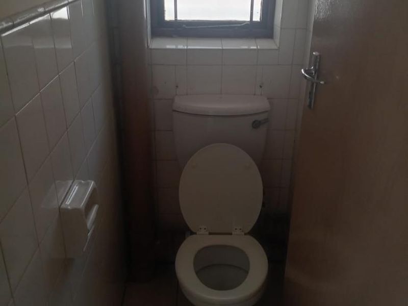 A compact bathroom featuring a standard toilet, tiled walls, and a small window providing natural light.