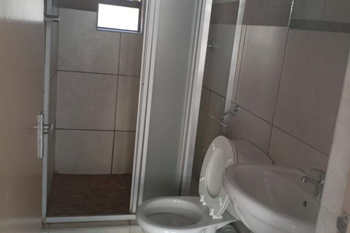 A functional bathroom featuring a pedestal basin, a standard toilet, and a shower enclosure with a tiled interior.