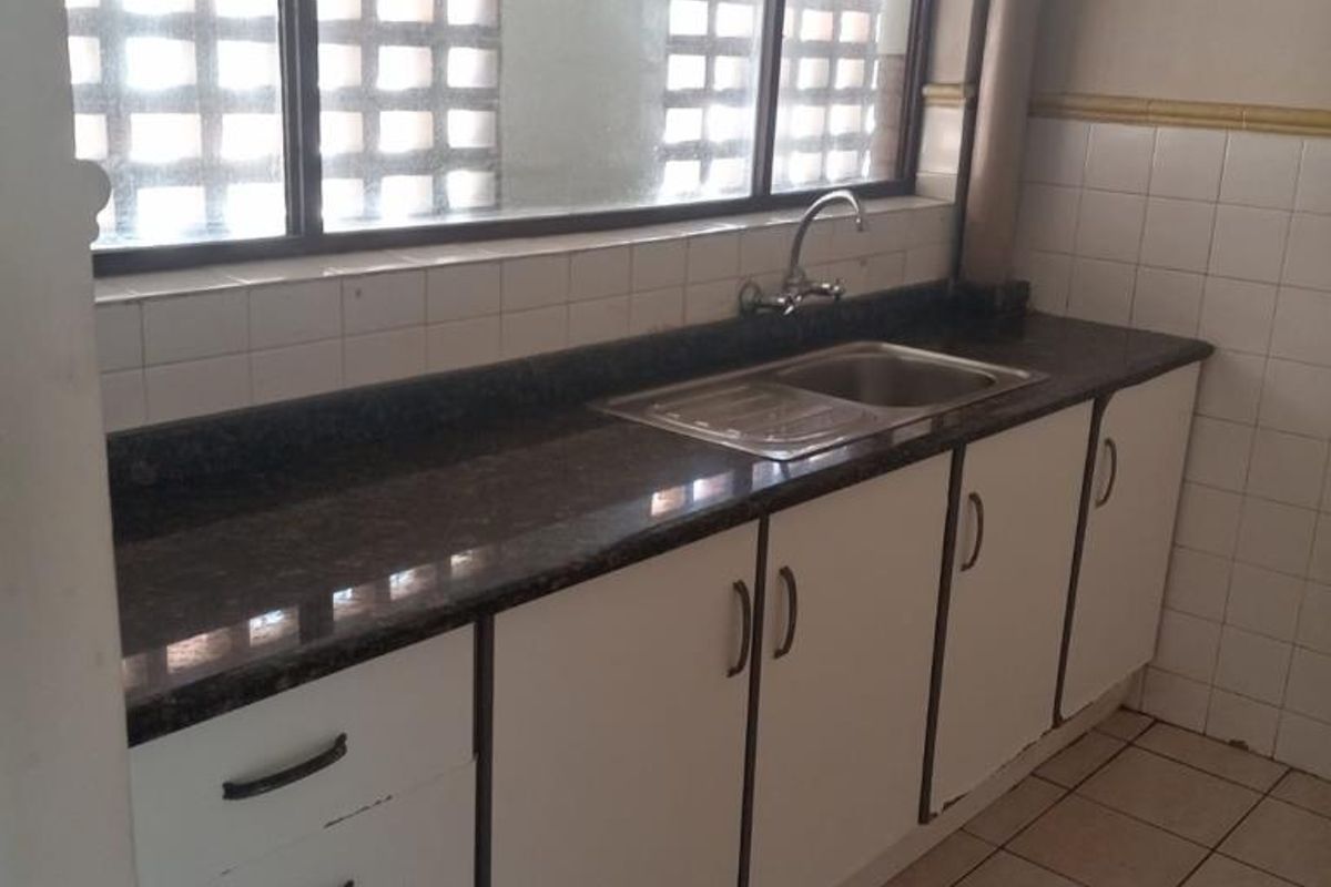 A functional kitchen area featuring dark granite countertops, white cabinetry, a stainless steel sink, and tiled flooring with a large window.