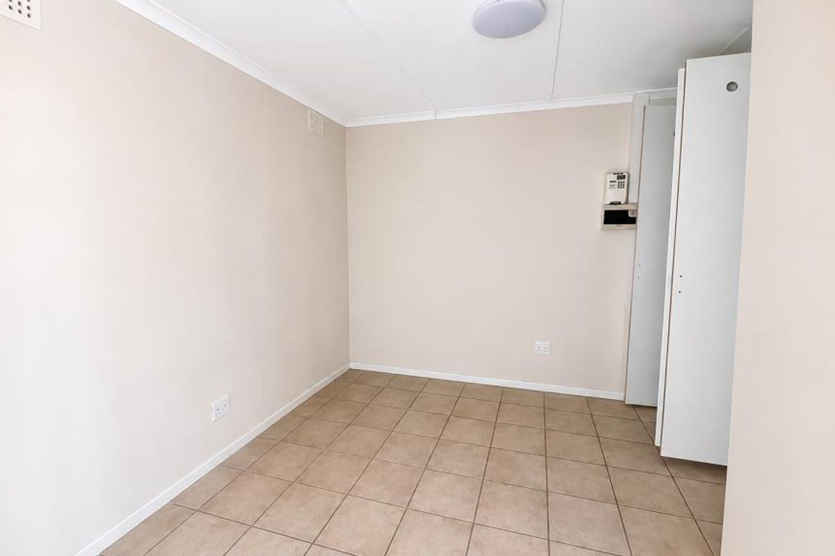 A clean, empty bedroom featuring neutral walls, tiled flooring, and built-in storage cupboards, providing a versatile space ready for personalization.