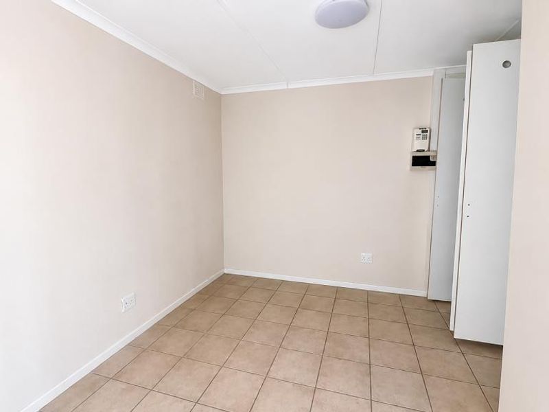 A clean, empty bedroom featuring neutral walls, tiled flooring, and built-in storage cupboards, providing a versatile space ready for personalization.
