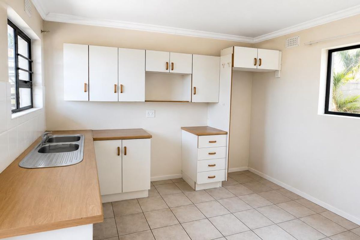 A clean, empty kitchen featuring white cabinetry, laminate countertops, a stainless steel double sink, and neutral tiled flooring.