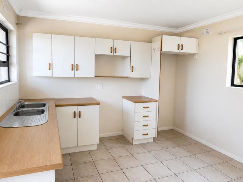 A clean, empty kitchen featuring white cabinetry, laminate countertops, a stainless steel double sink, and neutral tiled flooring.