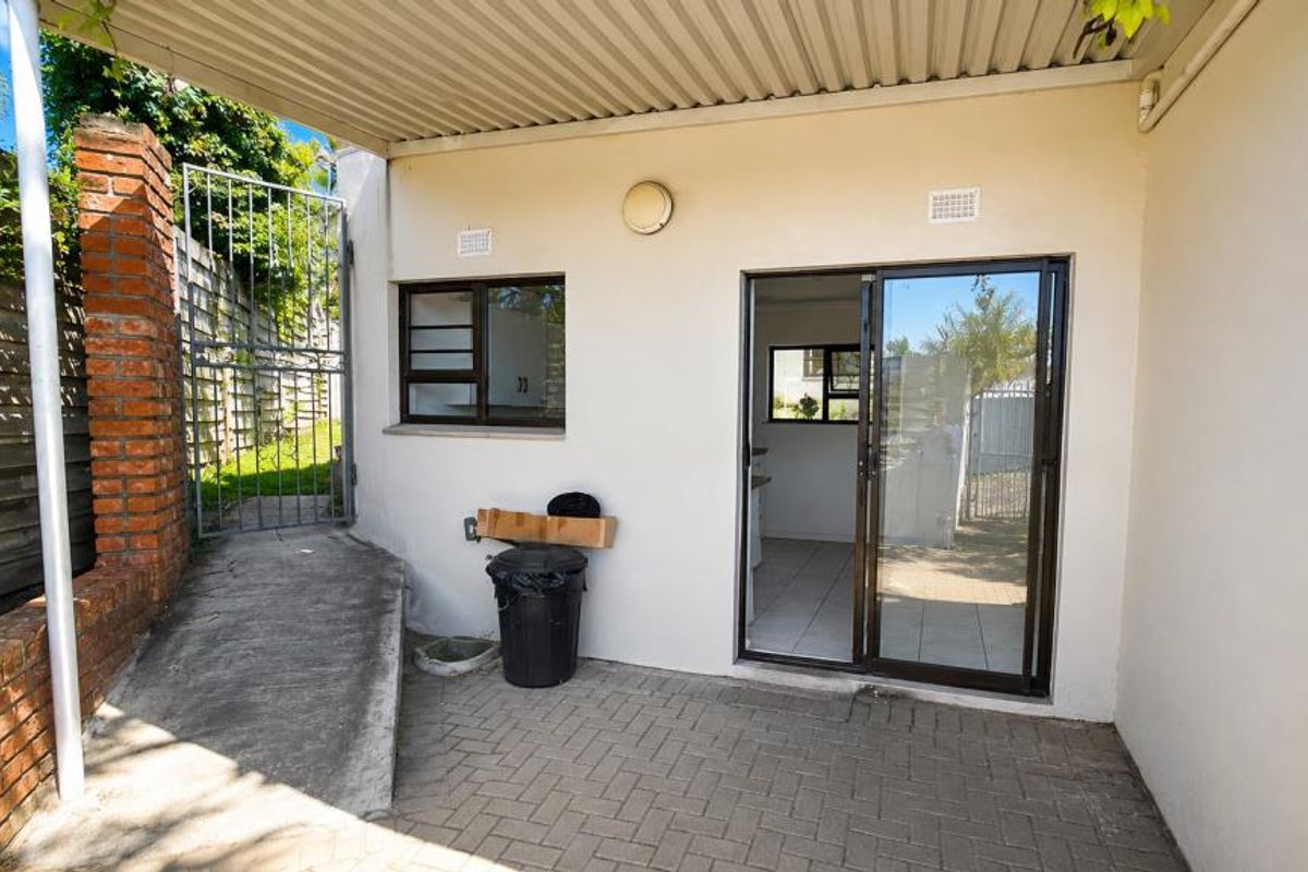Rear exterior view of the apartment featuring a paved patio area, concrete access ramp, sliding door entry, and a covered outdoor space.