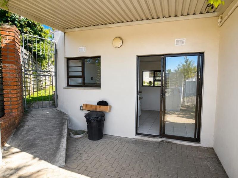 Rear exterior view of the apartment featuring a paved patio area, concrete access ramp, sliding door entry, and a covered outdoor space.