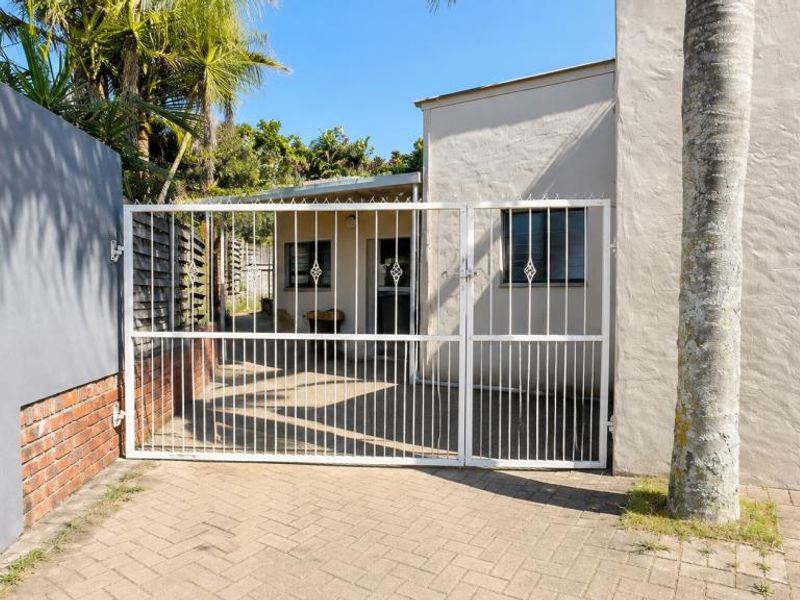 Front entrance view of the apartment featuring a paved driveway, secure metal gate, and garage access.