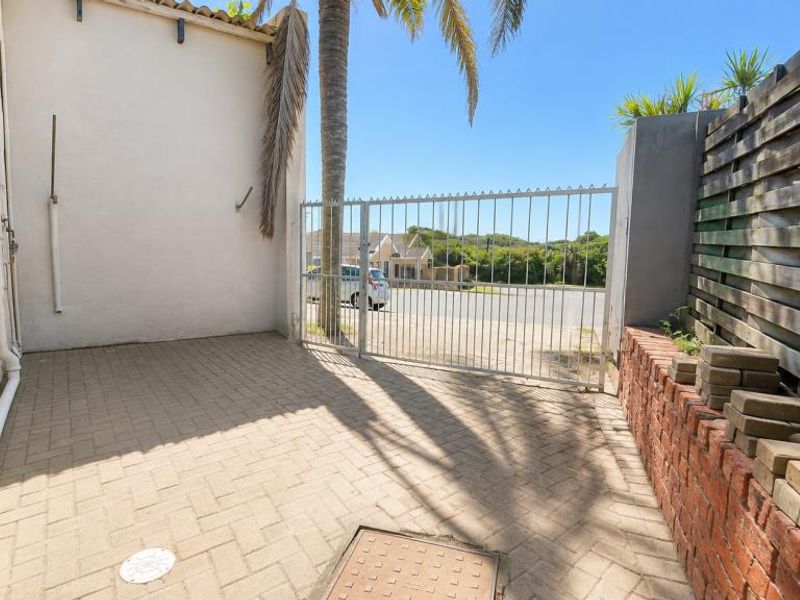 A paved rear courtyard area featuring a metal security gate, brick retaining wall, and timber fencing, providing a functional outdoor space.