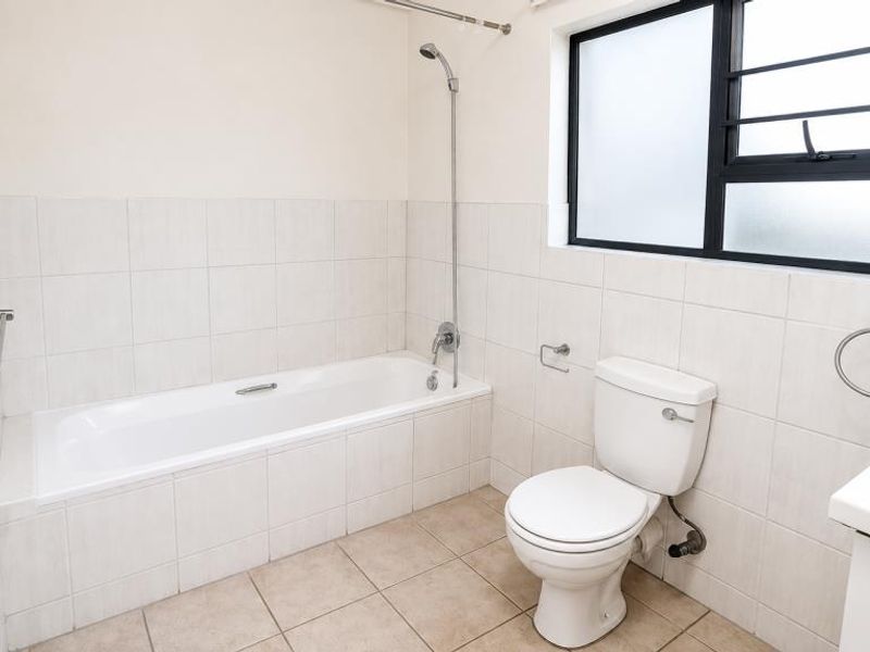 A clean, functional bathroom featuring a bathtub with shower attachment, a standard toilet, and neutral tiled finishes throughout.