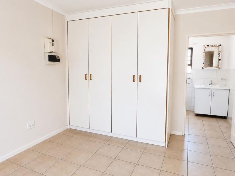 A clean, empty bedroom featuring tiled flooring, built-in cupboards, and direct access to an en-suite bathroom.