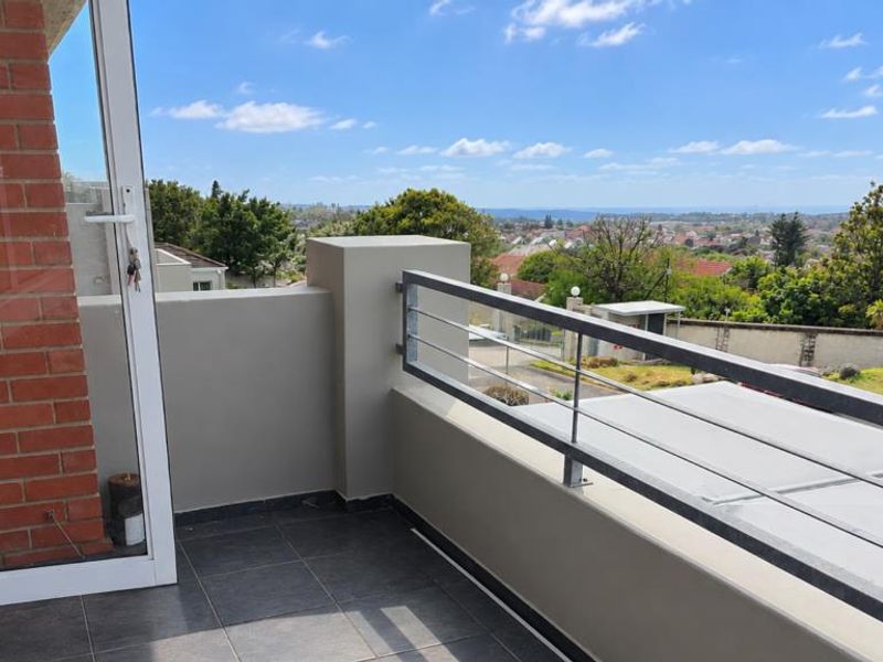 A clean, elevated balcony featuring tiled flooring, a modern metal railing, and expansive views of the surrounding neighborhood.