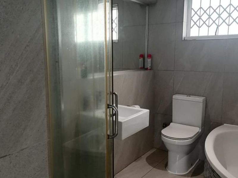 A functional bathroom featuring a shower enclosure, bathtub, wall-mounted basin, and toilet, finished with neutral wall and floor tiling.