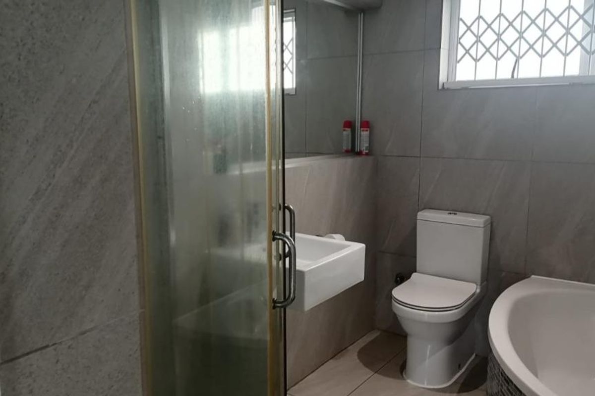 A functional bathroom featuring a shower enclosure, bathtub, wall-mounted basin, and toilet, finished with neutral wall and floor tiling.