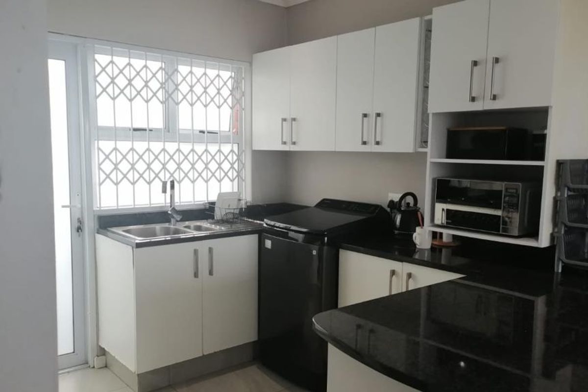 A functional kitchen featuring white cabinetry, dark granite countertops, a stainless steel sink, and a security gate on the window.