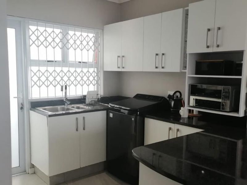 A functional kitchen featuring white cabinetry, dark granite countertops, a stainless steel sink, and a security gate on the window.