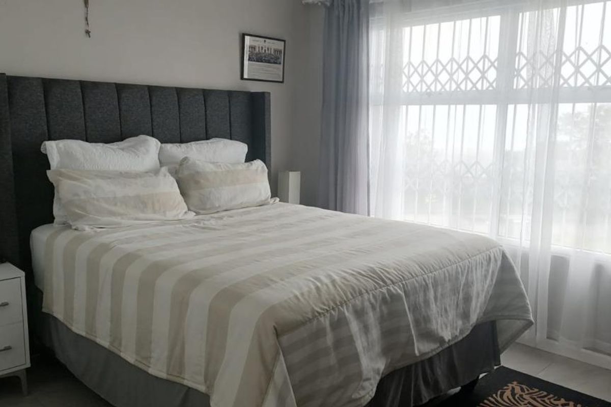 A well-maintained bedroom featuring tiled flooring and a large window fitted with a security gate for added safety.
