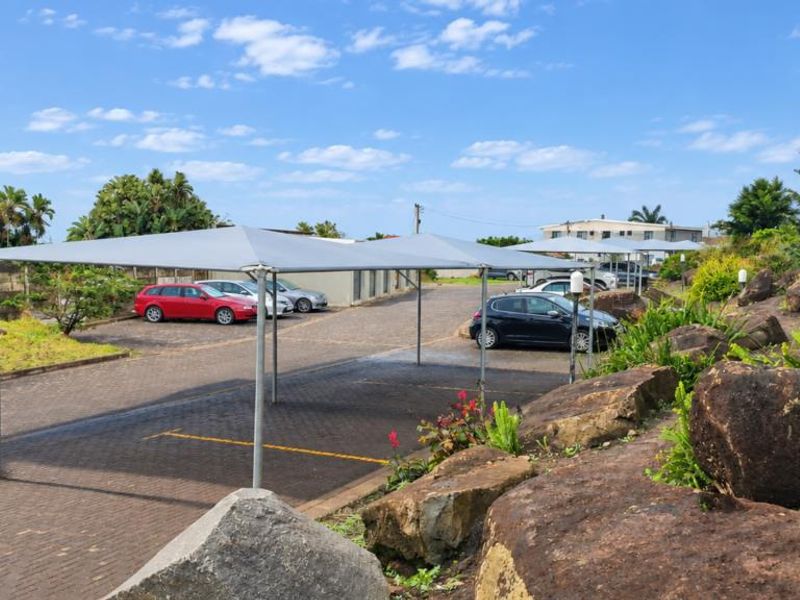 Exterior view of the townhouse complex featuring a paved driveway with shade cloth carports and landscaped rock garden areas.