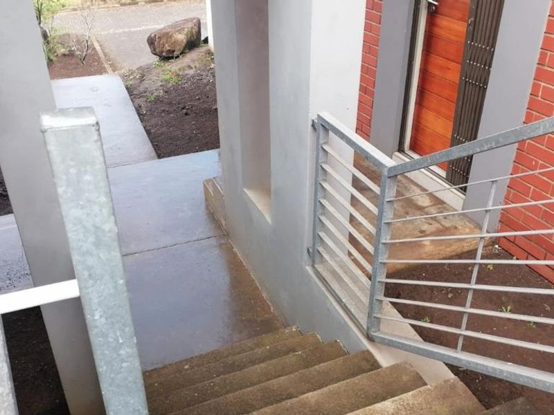 An exterior view of the townhouse entrance featuring a concrete staircase with metal balustrades leading to a timber front door and brick facade.