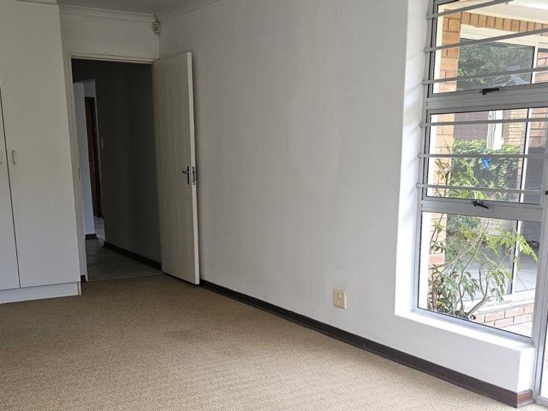 A vacant bedroom featuring built-in cupboards, carpeted flooring, and large windows with security bars, offering a bright and functional space.
