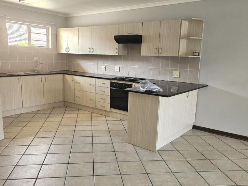 A clean, functional kitchen featuring light wood-finish cabinetry, dark countertops, tiled backsplash, and ceramic floor tiles, offering a neutral space ready for personalization.