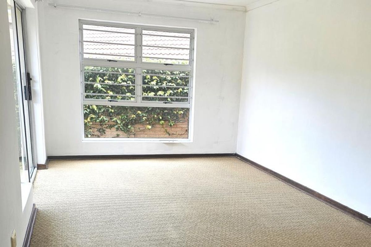 An empty bedroom featuring carpeted flooring, security bars on the window, and a sliding glass door providing access to the exterior.