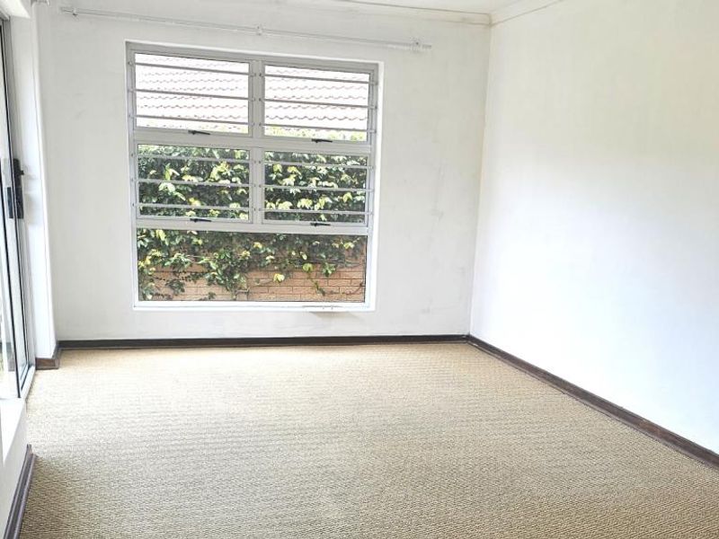 An empty bedroom featuring carpeted flooring, security bars on the window, and a sliding glass door providing access to the exterior.