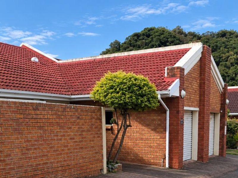 Front exterior view of a face brick townhouse featuring a red tiled roof, white gutters, and double roller shutter garage doors.