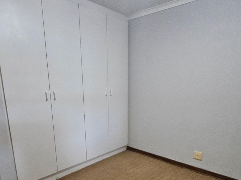 A clean, empty bedroom featuring neutral walls, carpet flooring, and ample built-in cupboard storage space.