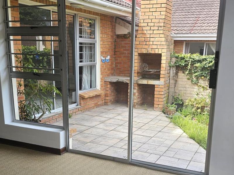 A paved outdoor patio area featuring a built-in brick braai, accessible through sliding glass doors from the interior living space.