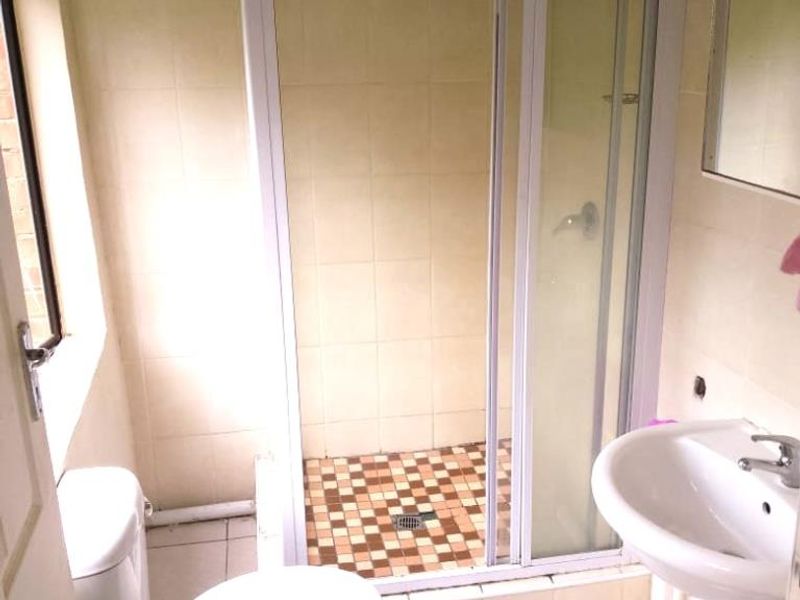 A compact bathroom featuring a shower cubicle with glass door, pedestal basin, and toilet, finished with dated wall and floor tiling.