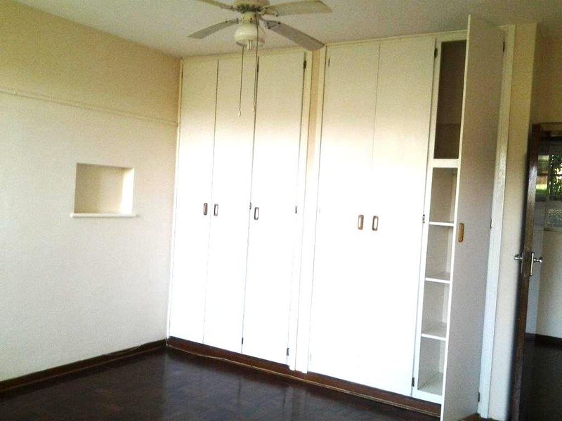 A vacant bedroom featuring built-in floor-to-ceiling cupboards, a ceiling fan, and original parquet flooring with a small decorative wall niche.