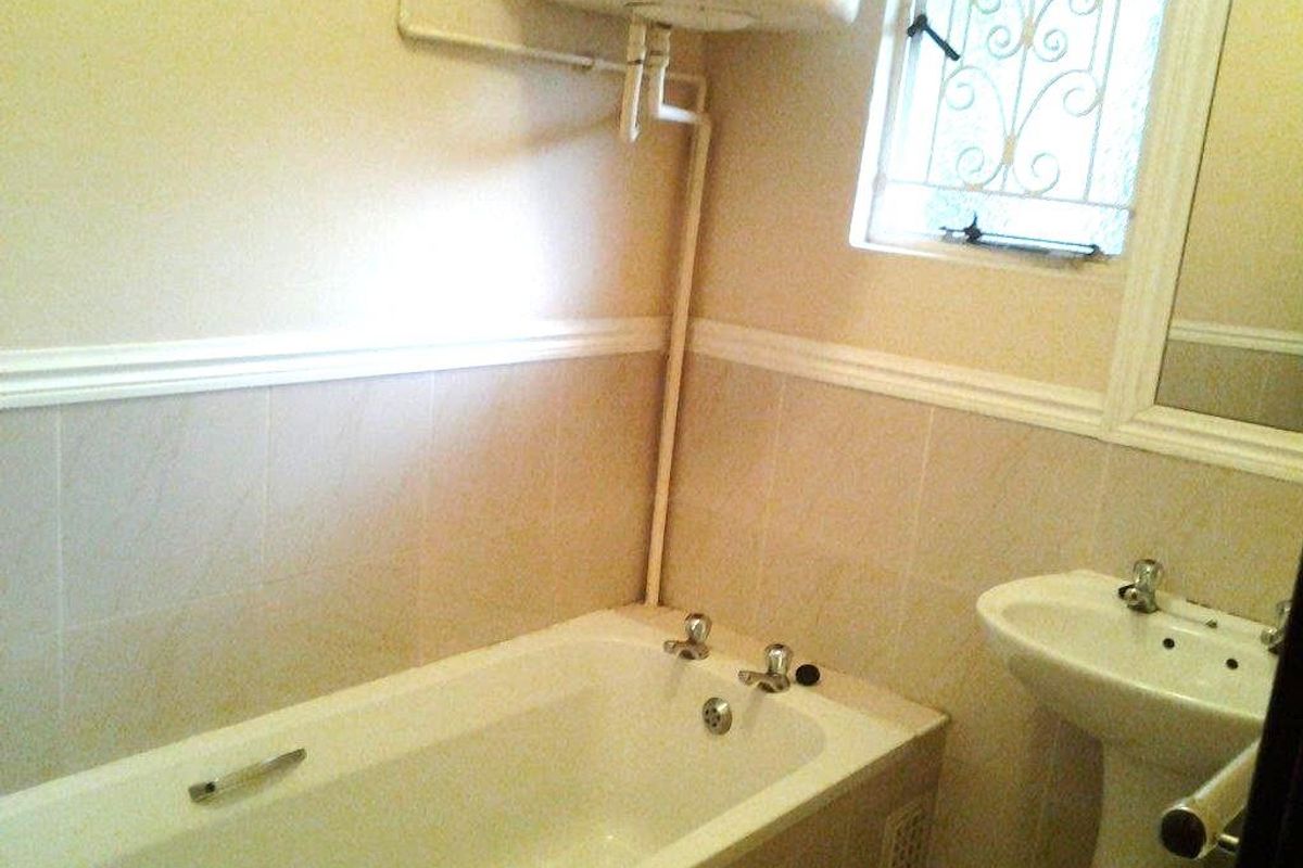 A dated bathroom featuring a standard bathtub, pedestal basin, and wall-mounted water heater with visible exposed plumbing.