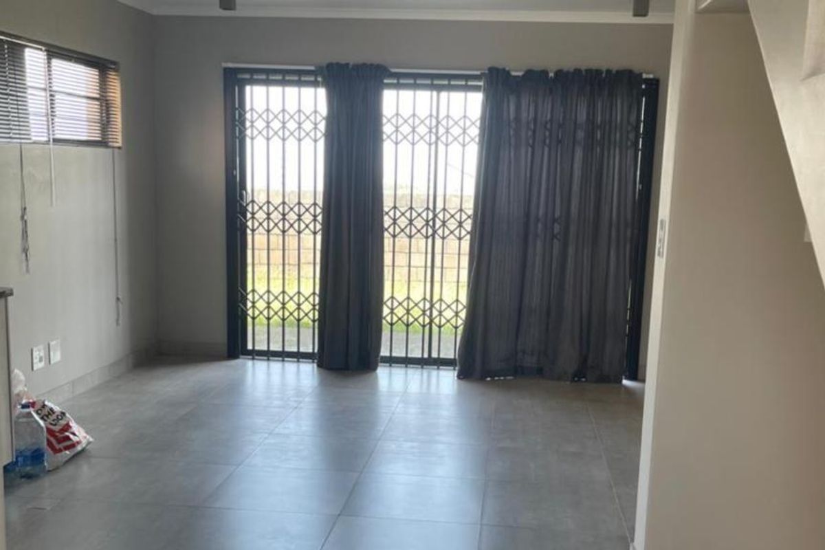 An open-plan living area featuring large format floor tiles, a sliding door with security gate, and access to an adjacent staircase.